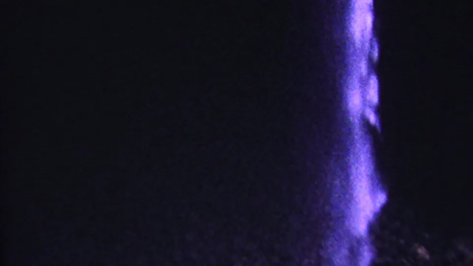 1962 Hawaii 8mm frame with a dim rocky surface and a vertical band of purple-lit falling water near the right side of the composition.