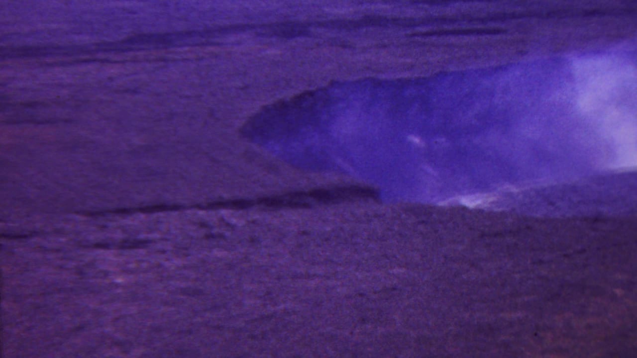 Steaming volcanic vent or crater opening in a barren rocky landscape.