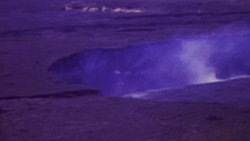 1962 Hawaii 8mm frame showing a wide view of a steaming volcanic vent or crater with white vapor rising from rugged barren terrain.