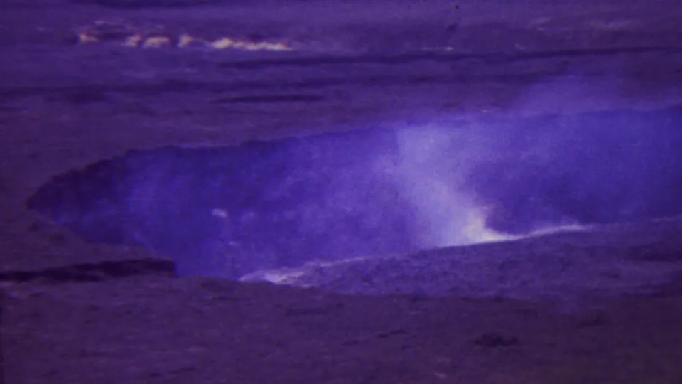 1962 Hawaii 8mm frame showing steam lifting from a large dark volcanic opening, with rough ground and distant sky softened by film grain and color drift.