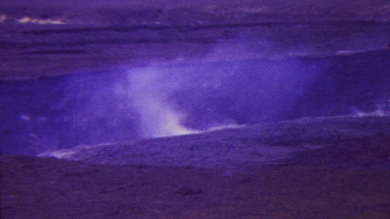 1962 Hawaii 8mm frame showing dark volcanic ground and a pale steam plume under a strong purple-blue film color cast.