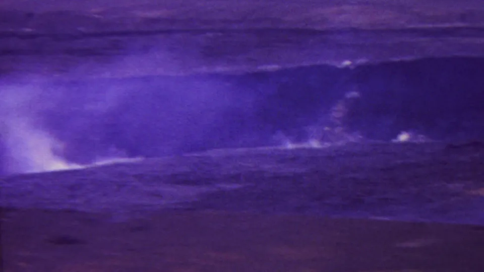 1962 Hawaii 8mm frame with a low volcanic fissure or vent releasing steam across dark open terrain, heavily tinted by aged film color.