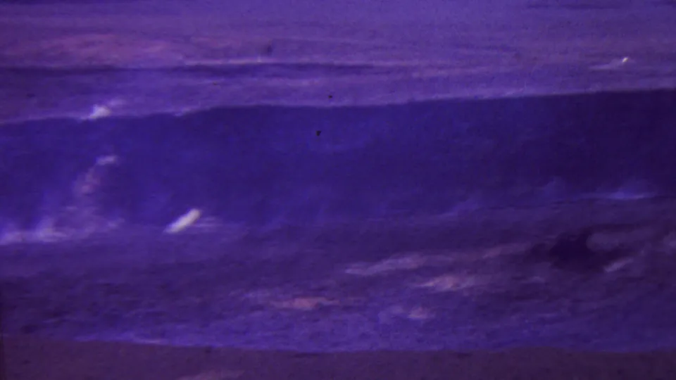 1962 Hawaii 8mm frame showing a broad volcanic field with faint steam, dark scorched-looking terrain, and pronounced magenta-blue film fading.