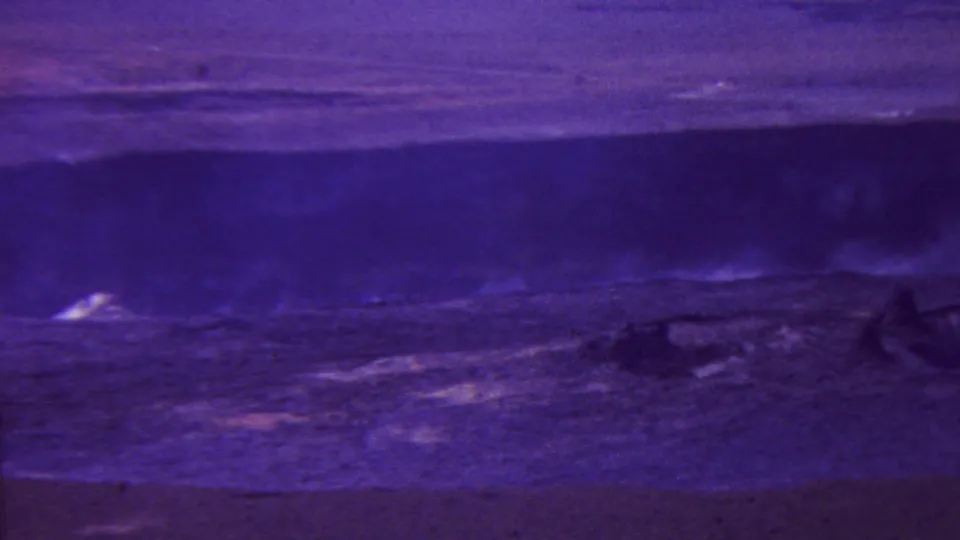 1962-attributed Hawaii 8mm frame showing a dark violet volcanic or coastal landscape with pale steam or surf-like plumes and heavy film grain.