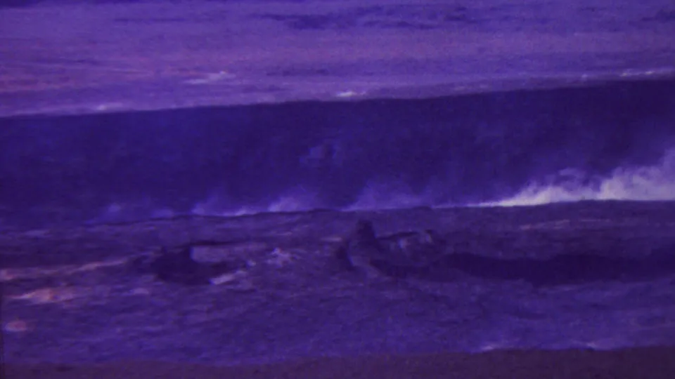 1962-attributed Hawaii 8mm frame showing a bright pale plume or surf break against a dark violet landscape, with the foreground largely in shadow.