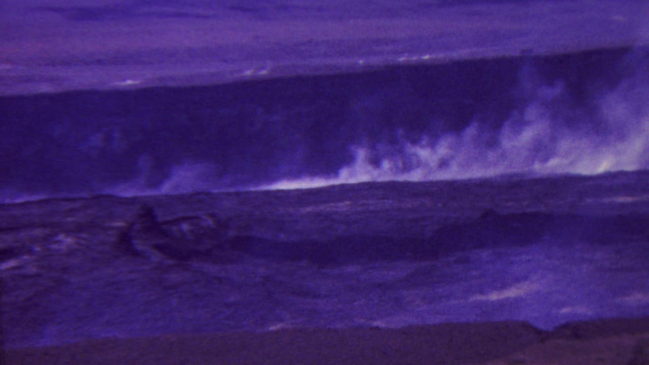 1962 Hawaii 8mm frame showing rough water, dark volcanic rock, and smoke or steam rising across a barren coastal crater landscape.