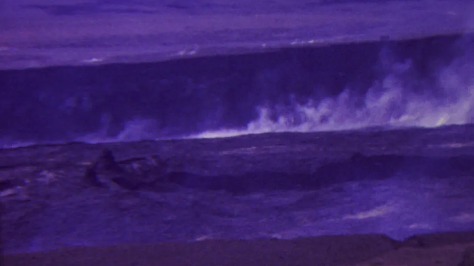 1962 Hawaii 8mm frame showing rough water, dark volcanic rock, and smoke or steam rising across a barren coastal crater landscape.