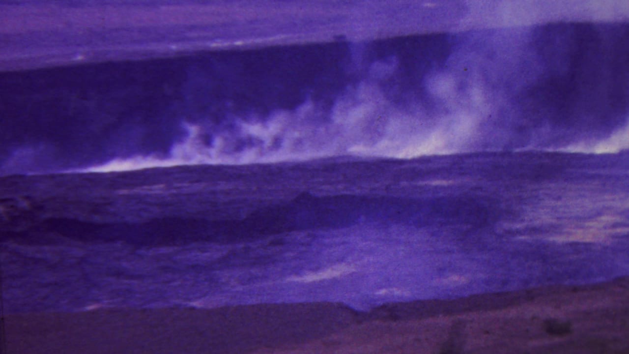 1962 Hawaii 8mm frame with a broad plume of smoke or steam drifting above black volcanic ground and foaming coastal water.