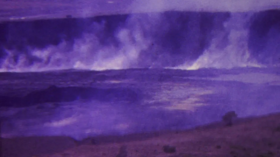 1962 Hawaii 8mm frame showing thick smoke or steam rising from a dark crater-like shoreline with rough water and empty volcanic terrain in front.