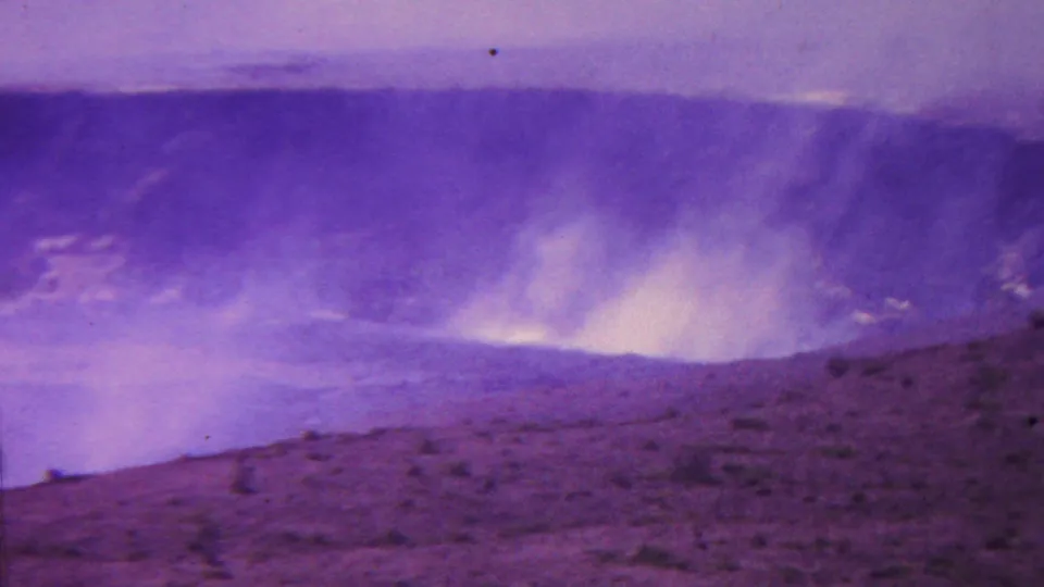1962 Hawaii 8mm frame showing dense smoke or steam lifting from the crater floor, with barren volcanic terrain crossing the foreground.