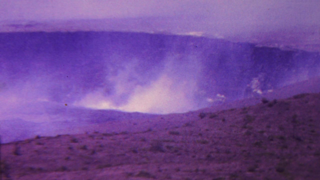 1962 Hawaii home-movie frame showing pale smoke or steam lifting from a broad crater area with purple-shifted film color.