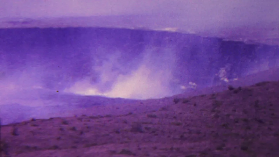 1962 Hawaii home-movie frame showing pale smoke or steam lifting from a broad crater area with purple-shifted film color.