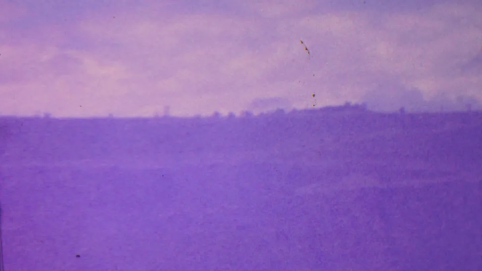 1962 Hawaii home-movie frame where haze and color shift obscure a distant crater or ridge line, with a low horizon and open sky.