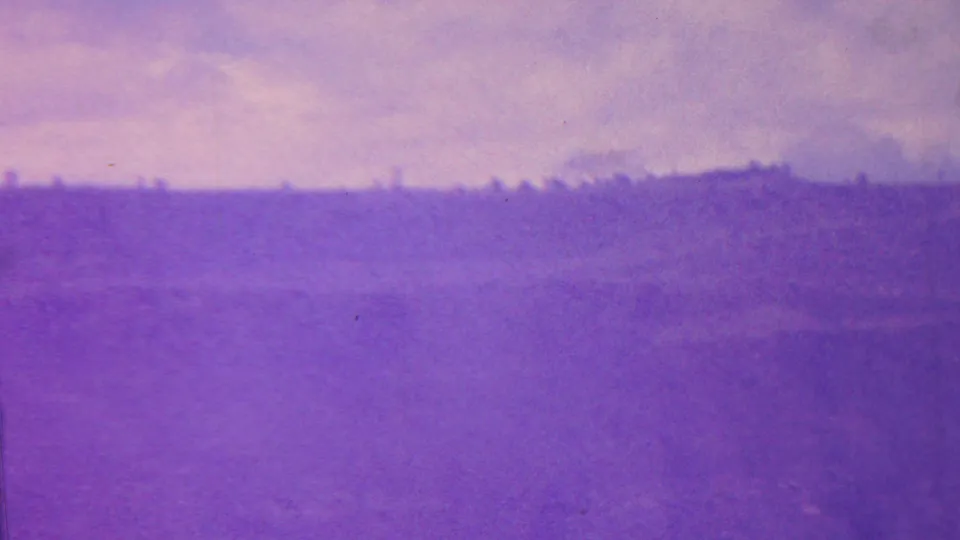1962 Hawaii 8mm frame showing a distant crater rim or ridge softened by haze, grain, and strong purple color shift.
