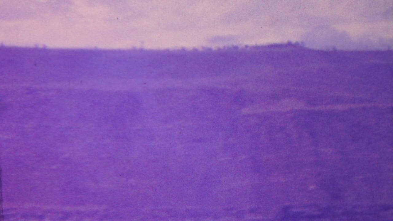 1962 Hawaii home-movie frame showing a purple-tinted canyon or valley landscape with a distant ridge line, open sky, and soft, grainy terrain detail.
