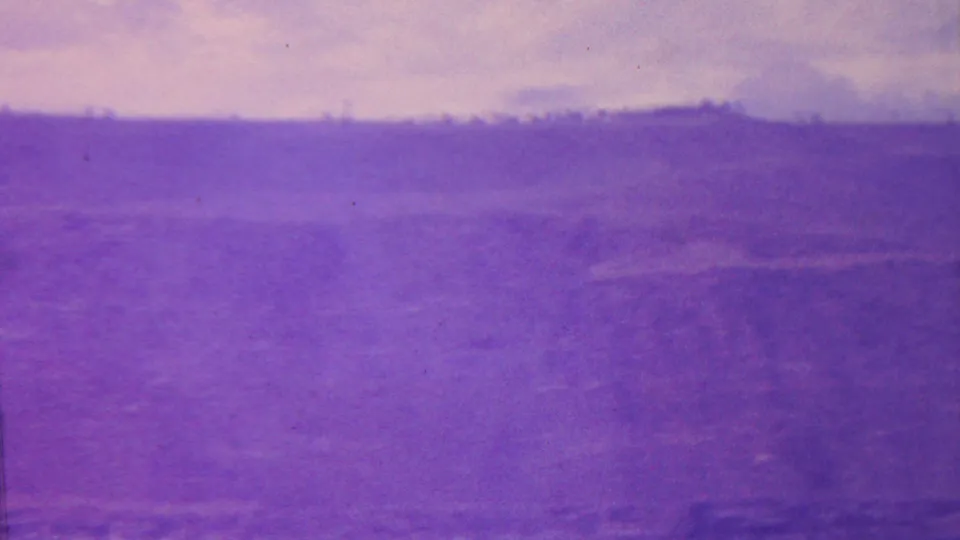 1962 Hawaii home-movie frame showing a purple-tinted canyon or valley landscape with a distant ridge line, open sky, and soft, grainy terrain detail.