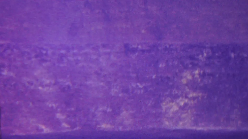 1962 Hawaii home-movie frame with a soft purple cast over a broad canyon wall or hillside, with indistinct vegetation and rock texture across the distance.