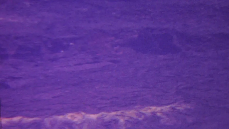 Purple-tinted 1962 Hawaii 8mm frame showing a close view of rippled water or wet ground with soft pale reflections and dark surface patches.