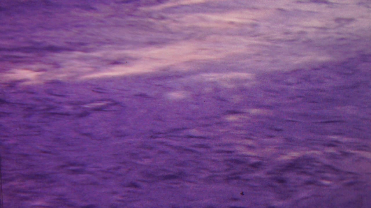 1962 Hawaii 8mm frame showing a close, purple-shifted view of rugged rock or ground texture with light streaks across the surface.