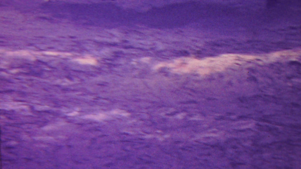 Close terrain surface with purple cast and lighter bands across rough texture.
