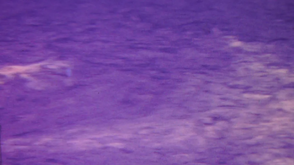 1962 Hawaii 8mm frame of textured terrain or rock face with a strong purple cast, faint pale markings, and visible home-movie grain.