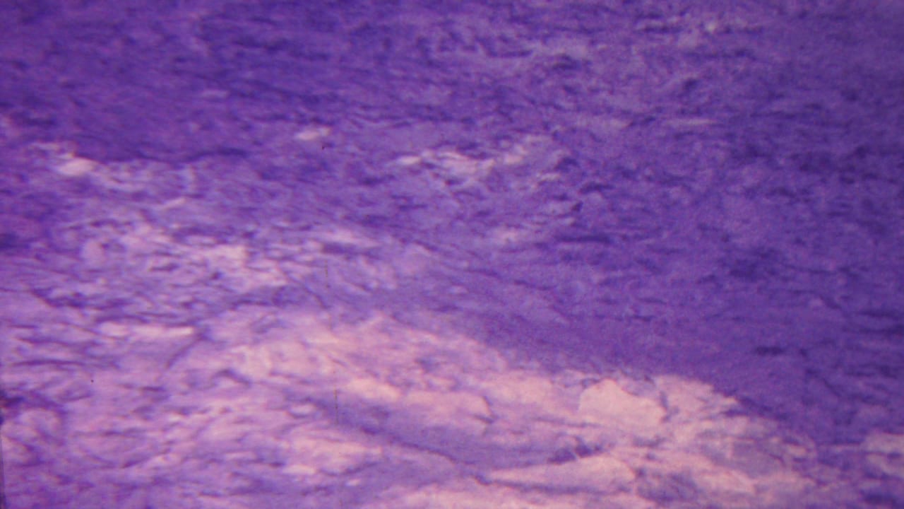 1962 Hawaii 8mm frame showing a purple-tinted sky above textured volcanic ground with visible grain and soft exposure.
