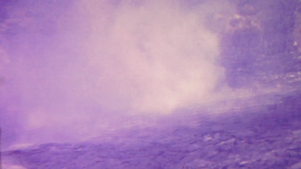 1962 Hawaii 8mm frame with a pale steam plume rising from dark volcanic ground beneath a magenta-purple sky.