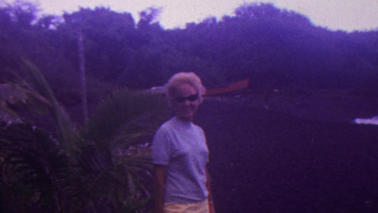 In supplied 1962 Hawaii 8mm footage, a woman with short blonde hair and sunglasses stands near palm-like plants and dense greenery.