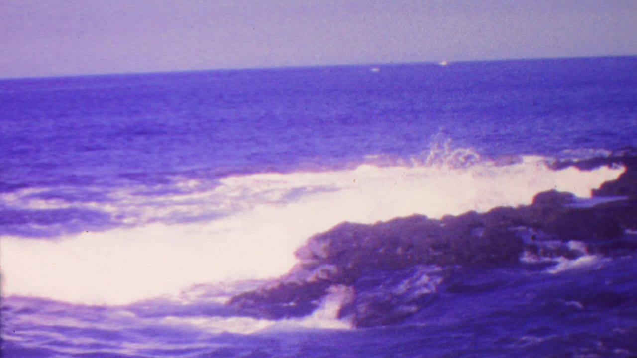 A wave crashes against a rocky outcrop with spray and white foam.