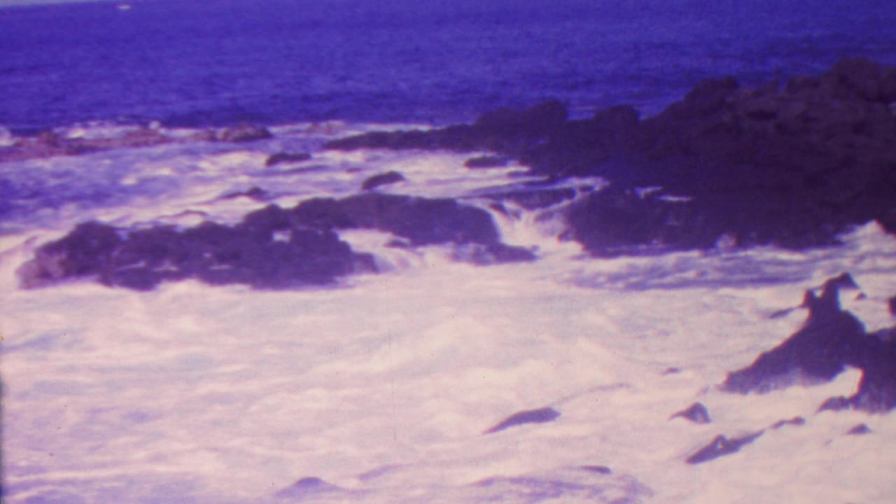 Foamy ocean water washes around jagged rocks near the shoreline.