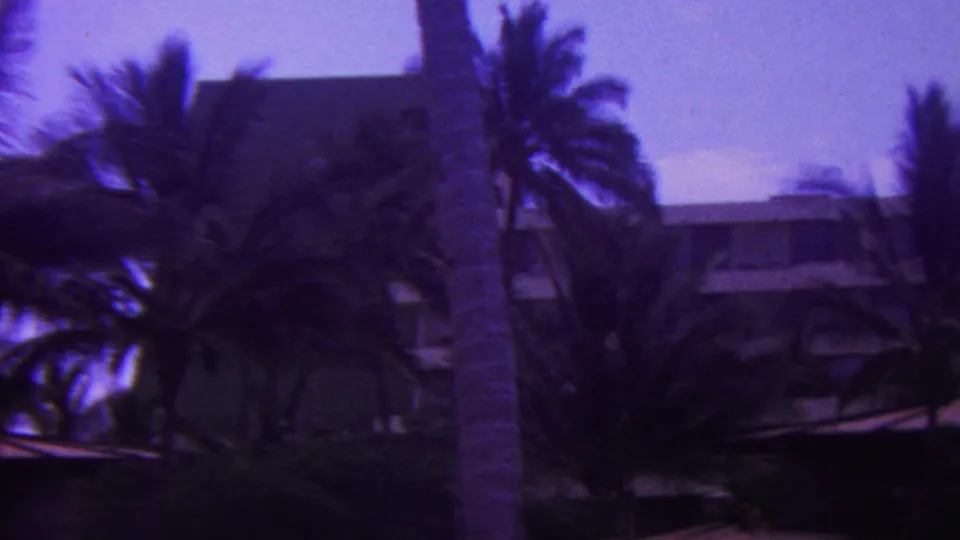 1962 Hawaii 8mm frame showing several palm trees and a partially visible white multi-level resort-style building in the background.