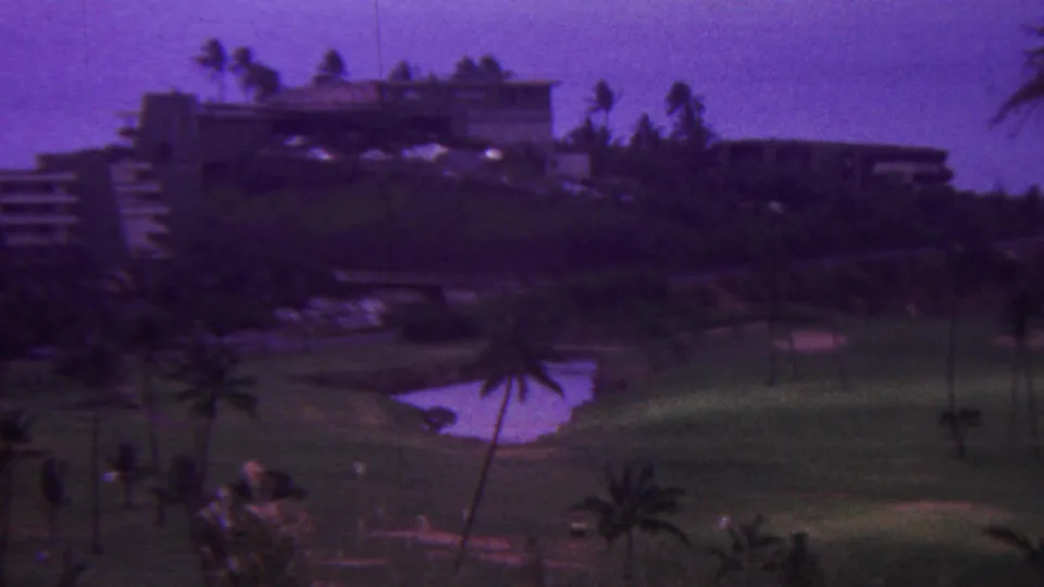 1962 Hawaii home-movie frame showing a manicured golf-course area with a small pond, scattered palms, and resort buildings above the lawn.