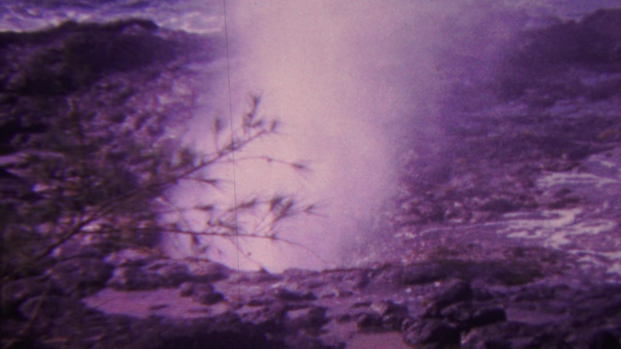 1962 Hawaii 8mm frame of a coastal blowhole-like spray plume rising from dark rocks as surf moves across the shoreline.