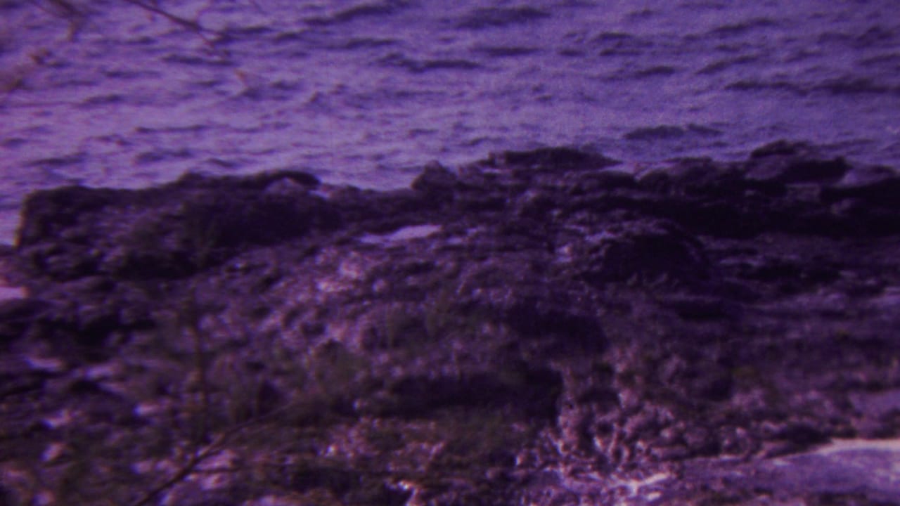1962 Hawaii 8mm frame of a rugged rock shelf at the waterline with rippled ocean beyond and aged purple-magenta color shift.