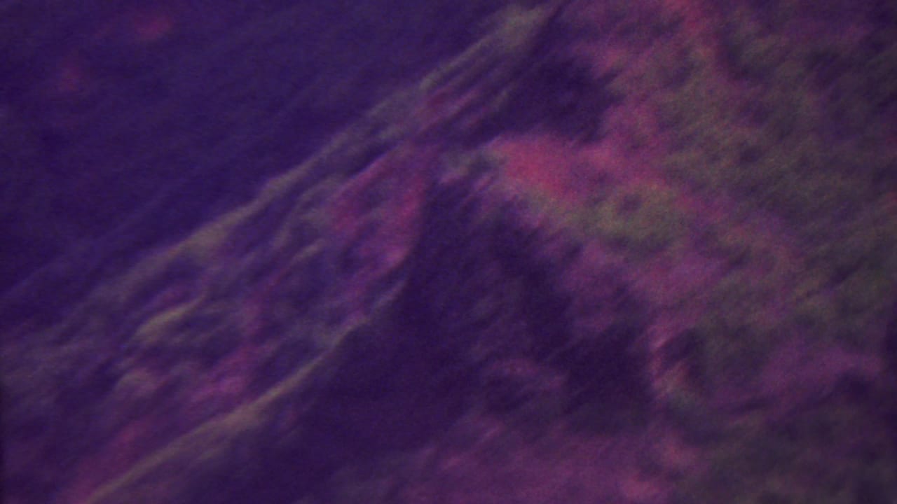 Blurred panning view of dark hillsides and red earth with vegetation.