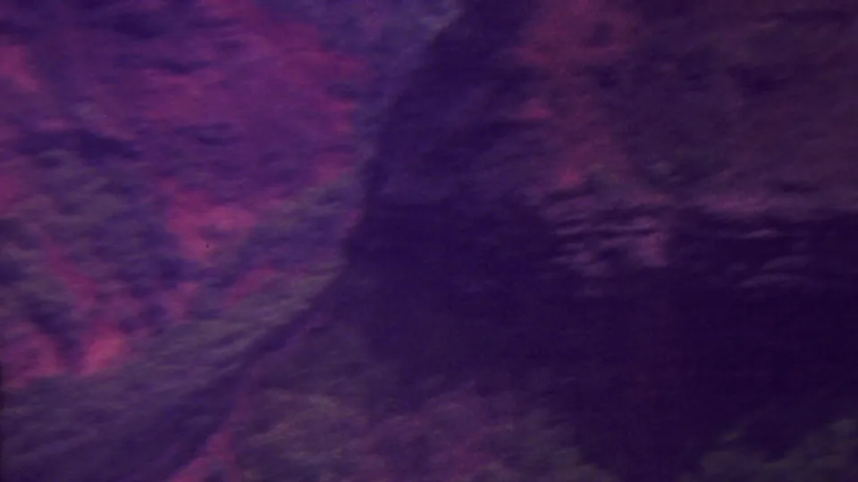 1962 Hawaii 8mm frame showing textured red and purple rock formations, a dark ravine, and green vegetation along the lower edge.