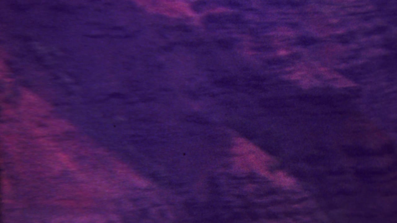 High-vantage 8mm view across rugged Hawaiian mountain ridges and dark ravines, with strong purple-magenta color saturation.