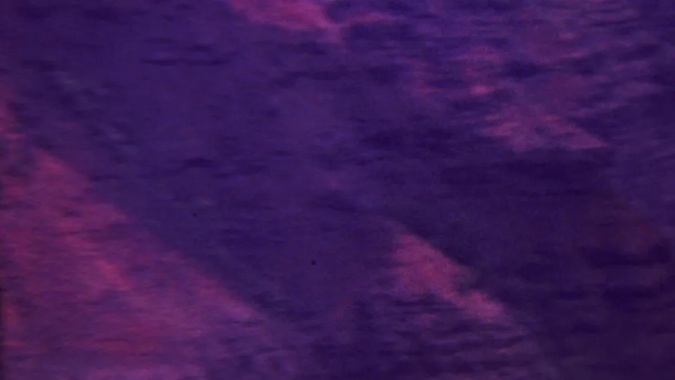High-vantage 8mm view across rugged Hawaiian mountain ridges and dark ravines, with strong purple-magenta color saturation.