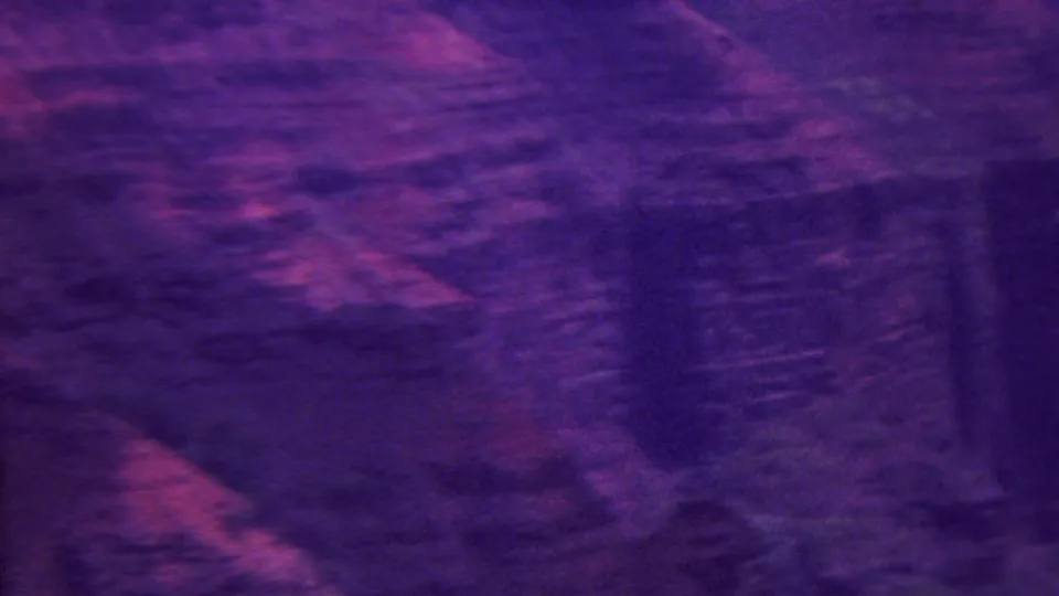 1962 Hawaii home-movie frame with blurred overhead terrain, textured rock faces, and saturated purple film tones.