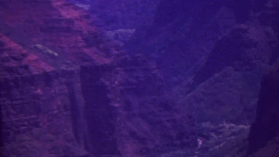 Final 8mm frame looking across a dark mountain wall or valley edge in Hawaii, rendered with deep purple and magenta home-movie color shift.
