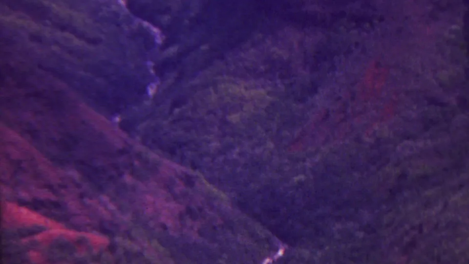 1962 Hawaii vacation footage frame looking down into a forested canyon valley where a small bright stream traces through dark slopes.