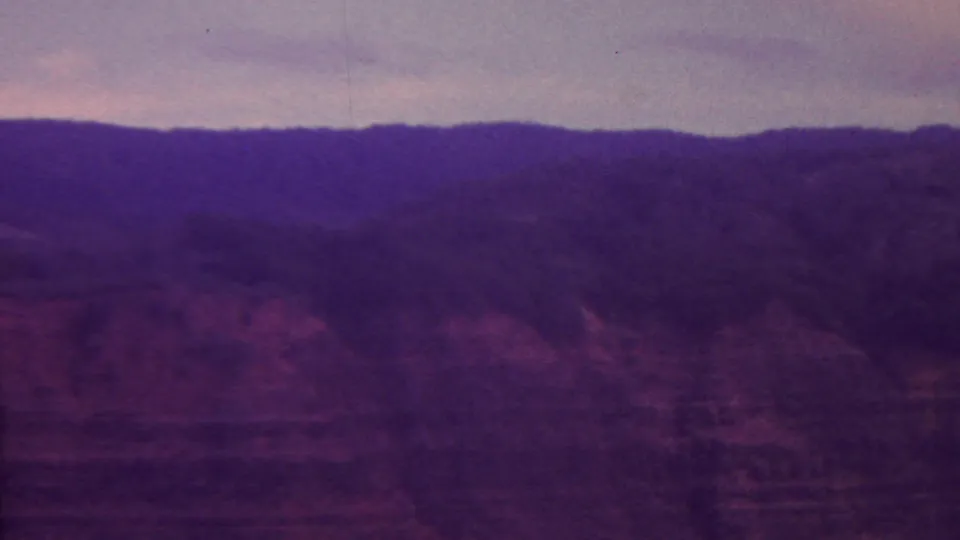 1962 Hawaii 8mm frame showing dark mountain ridges and valley terrain, with a faint pale line that appears to be a river or stream below.