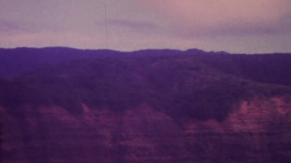 A source-attributed 1962 Hawaii 8mm frame showing layered reddish rock formations, dark upper slopes, and a hazy evening sky.
