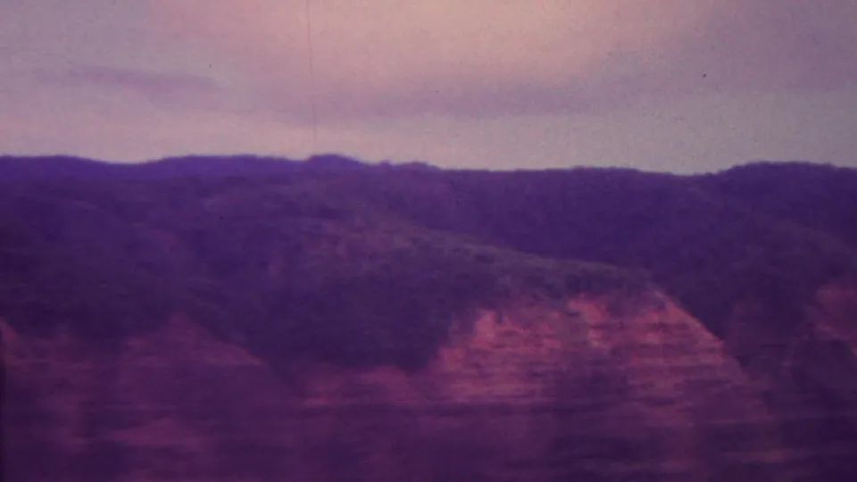 A vintage 8mm landscape frame from the supplied Hawaii 1962 metadata, with reddish canyon walls, dark hills, and a subdued purple-gray sky.