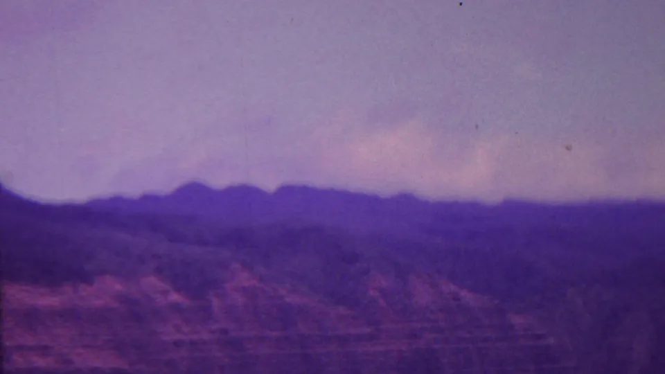 1962 Hawaii 8mm frame looking across hazy mountain ridges and darkened slopes beneath a pale cloudy sky.