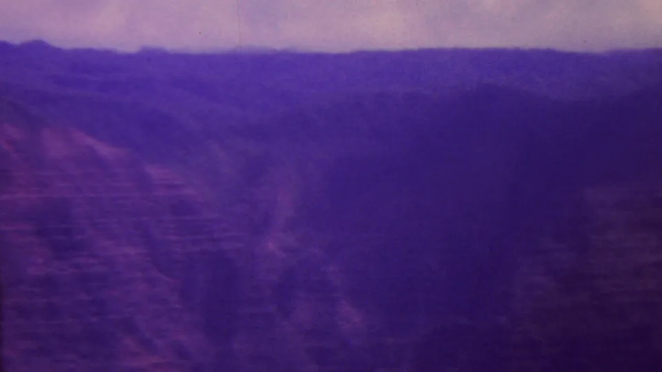 1962 Hawaii 8mm frame showing distant mountain ridges, dark canyon slopes, and a soft overcast sky with strong purple film fading.