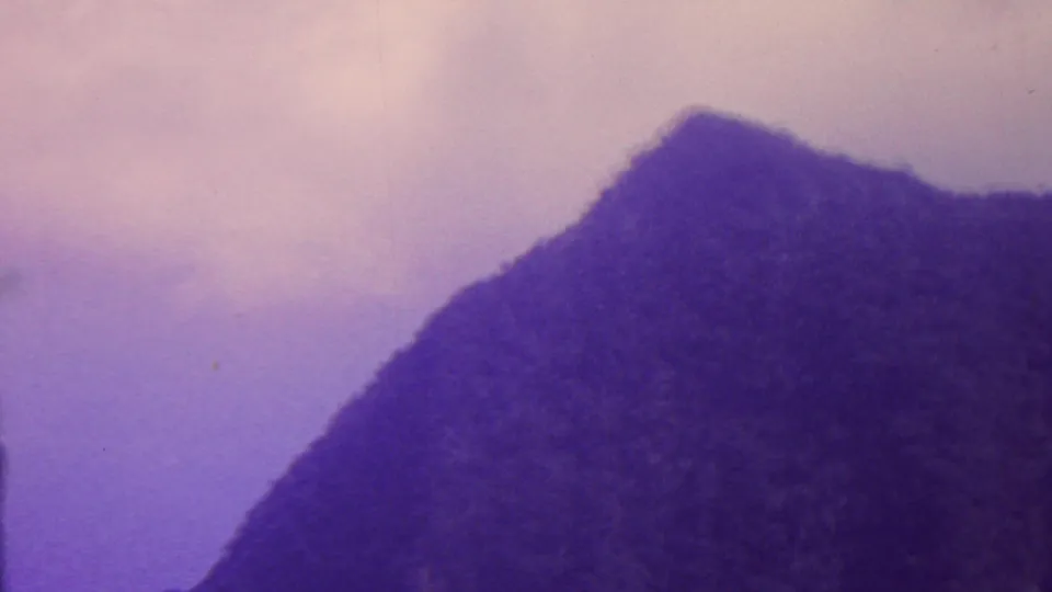 1962 Hawaii 8mm frame showing a steep mountain peak and dark vegetated slope against a pale, hazy sky with visible film grain.