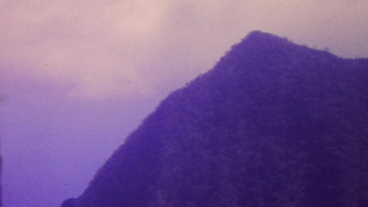 1962 Hawaii 8mm frame showing a shadowed mountain slope rising against a lavender-purple sky, with soft focus and visible film grain.