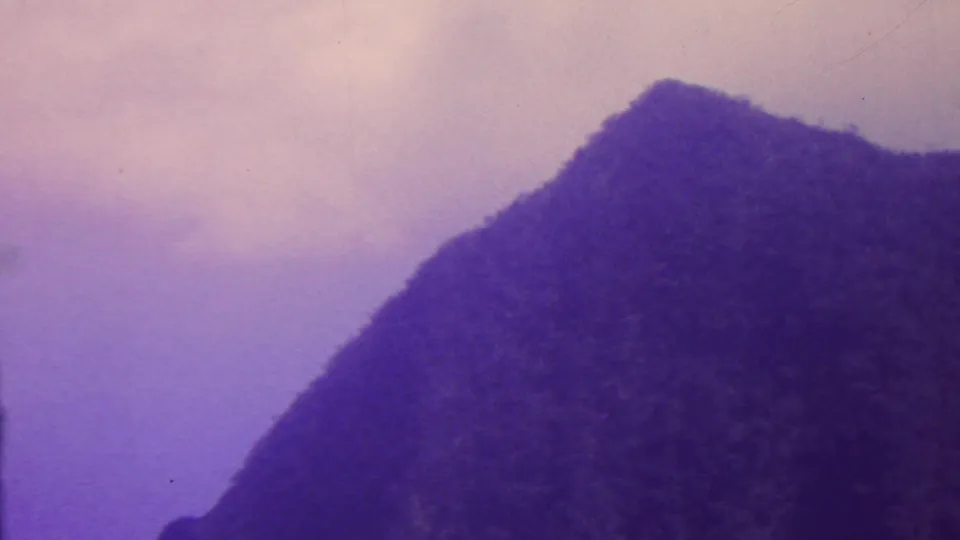 1962 Hawaii 8mm frame showing a shadowed mountain slope rising against a lavender-purple sky, with soft focus and visible film grain.