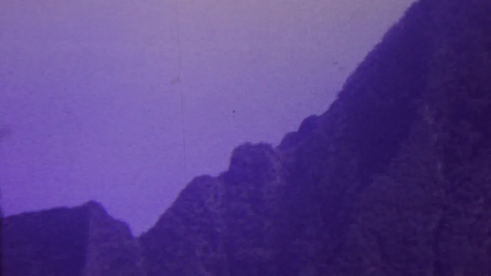 1962 Hawaii archival home-movie frame with dark ridges, a shadowed valley shape, and muted purple sky across a grainy 8mm scan.